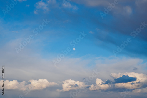 Cumulus, cirrocumulus clouds and full moon on blue sky background.