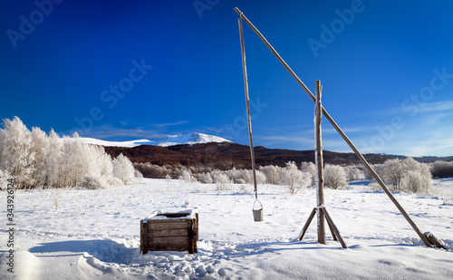 Fototapeta Naklejka Na Ścianę i Meble -  Frosty winter morning in the mountains (Bieszczady National Park). View of the well - crane in Wolosate village. In the background: Tarnica - the highest peak of the Bieszczady Mountains in Poland. 