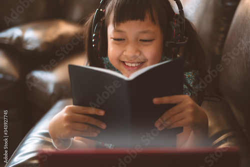 Happy little child girl lying on sofa with learning by laptop and writing a book at home,Social distance during quarantine, Online education concept