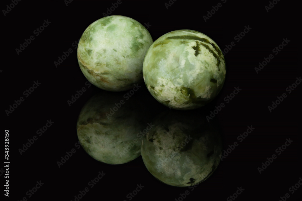 Fototapeta premium Two malachite balls, similar to two planets, lie on a glossy black glass, in which their reflection is visible