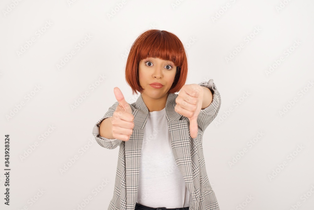 Pretty young pensive woman making good-bad sign. Displeased and unimpressed wearing casual clothes. Pretty young pensive woman making good-bad sign. Displeased and unimpressed wearing casual clothes.