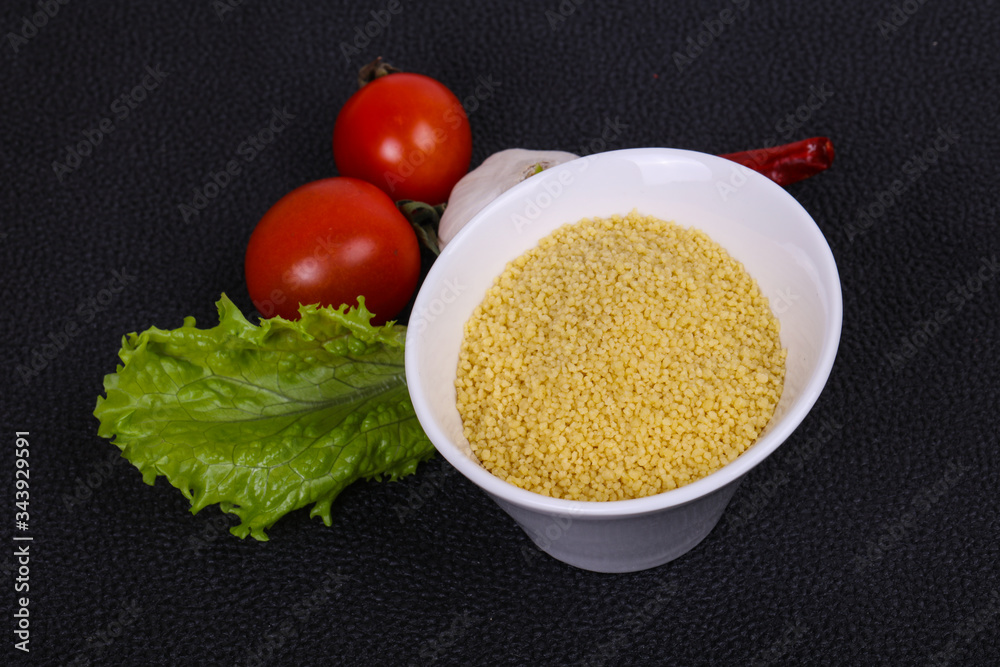 Raw couscous in the bowl served salad leaves, tomato and pepper