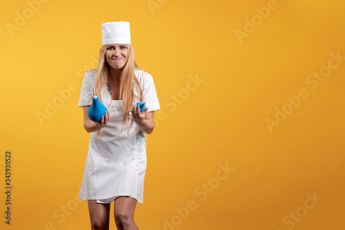 Obraz na plátne Emotional young woman doctor nurse in a white coat and hat with a douche enema i