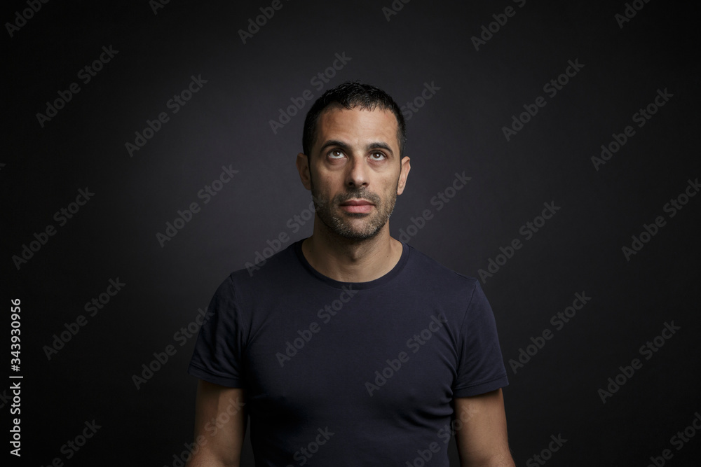uomo moro con maglia nera guarda serio verso l'alto , isolato su sfondo nero uomo moro con maglia nera guarda serio verso l'alto , isolato su sfondo nero