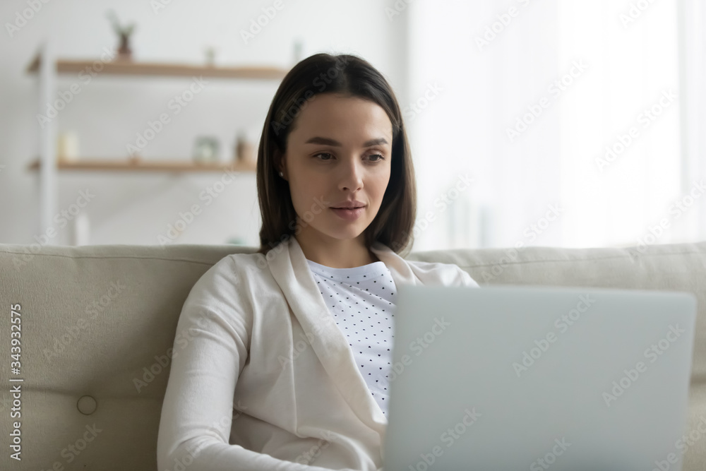 Millennial Caucasian girl sit relax on sofa ta home browsing wireless internet on computer, concentrated young woman working or studying on laptop in living room, shopping online, make purchase on web Millennial Caucasian girl sit relax on sofa ta home browsing wireless internet on computer, concentrated young woman working or studying on laptop in living room, shopping online, make purchase on web