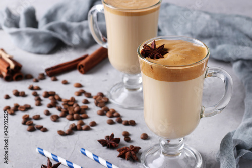 Iced Dalgona coffee in tall glasses with spices on light grey concrete background. Korean creamy whipped coffee trend, Copy space, Horizontal format