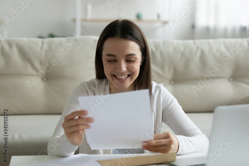 Happy millennial girl sit at home feel excited reading good news in postal paperwork letter, smiling young woman laugh enjoy pleasant positive response in post paper correspondence or notice