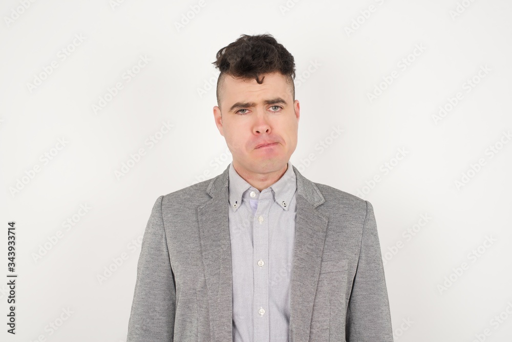 Pensive attractive blond male being deep in thoughts, raises eyebrows, curves lips, wears fashionable clothes, stands against gray wall with copy space for your text. Pensive attractive blond male being deep in thoughts, raises eyebrows, curves lips, wears fashionable clothes, stands against gray wall with copy space for your text.