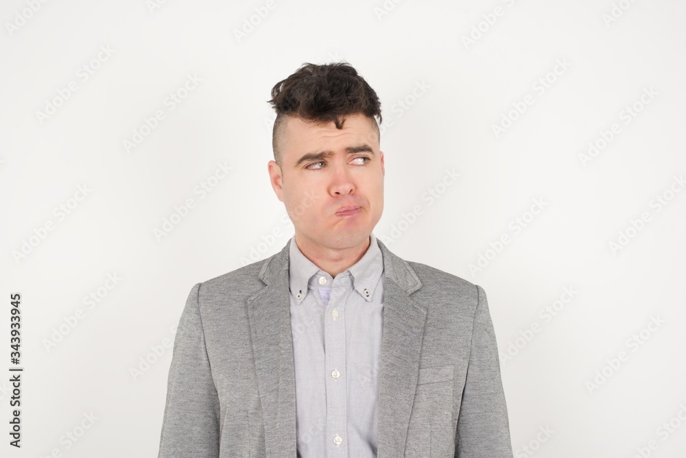Pleasant looking young male student, looks pensively aside, plans actions after university, imagines what to do. Clever man thinks over about new project. Copy space on gray. Pleasant looking young male student, looks pensively aside, plans actions after university, imagines what to do. Clever man thinks over about new project. Copy space on gray.