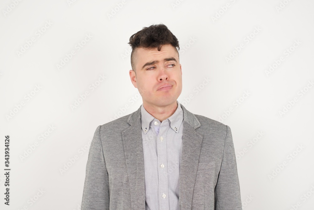 Troublesome puzzled Caucasian man frowns face, bites lip, raises eyebrows, looks up, has problems, dressed in fashionable clothes, isolated over gray background, has regret look. Troublesome puzzled Caucasian man frowns face, bites lip, raises eyebrows, looks up, has problems, dressed in fashionable clothes, isolated over gray background, has regret look.