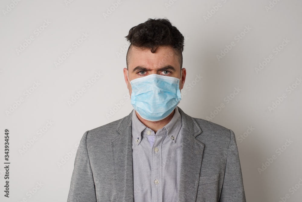 Portrait of outraged young man with oval face, blue eyes wearing medical mask frowning his eyebrows being displeased with something. Scowling pretty female isolated over grey. Portrait of outraged young man with oval face, blue eyes wearing medical mask frowning his eyebrows being displeased with something. Scowling pretty female isolated over grey.