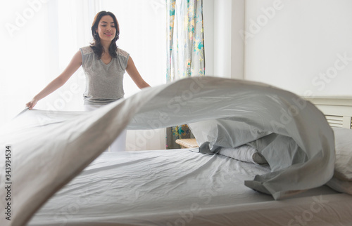 Young woman spreading sheet on bed