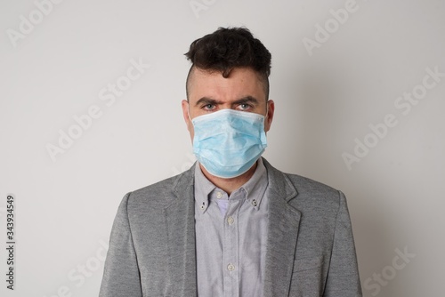 Portrait of outraged young man with oval face, blue eyes wearing medical mask frowning his eyebrows being displeased with something. Scowling pretty female isolated over grey.