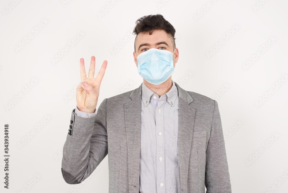 Young blond man standing standing against gray wall showing and pointing up with fingers number three while smiling confident and happy. Young blond man standing standing against gray wall showing and pointing up with fingers number three while smiling confident and happy.