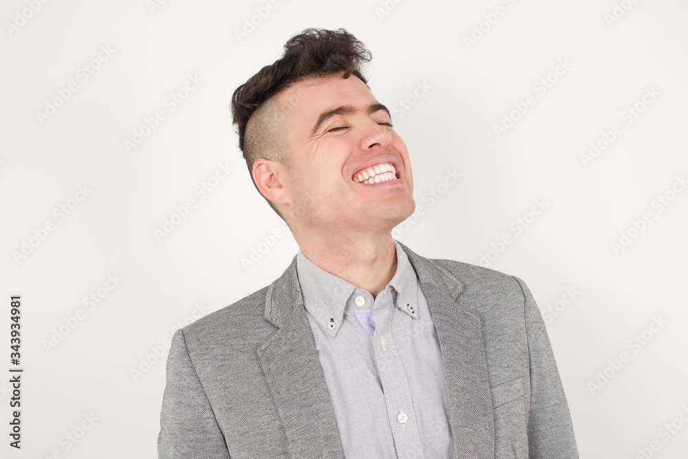 Joyful European man having fun and laughs at good joke or sings wears casual clothes, standing against gray wall. Happy man poses inddoors. Joyful European man having fun and laughs at good joke or sings wears casual clothes, standing against gray wall. Happy man poses inddoors.