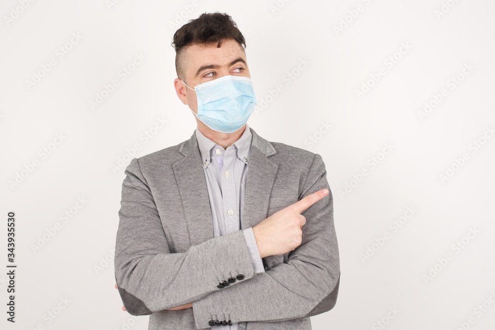 Portrait of young man wearing medical mask posing on camera with tricky look and gesturing to side. Male designer presenting lovely product with index finger. Gesture concept. Portrait of young man wearing medical mask posing on camera with tricky look and gesturing to side. Male designer presenting lovely product with index finger. Gesture concept.