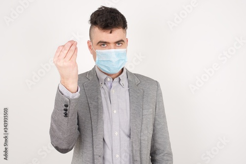 What the hell are you talking about. Shot of frustrated young European man wearing medical mask gesturing with raised hand doing Italian gesture, frowning, being displeased  with dumb question.