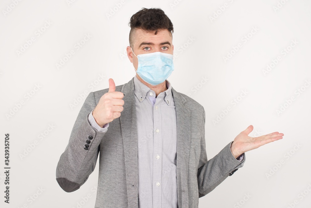 Young happy cheerful businessman showing thumb up and pointing with the other hand while standing indoors. Good Job. Wearing casual clothes. Young happy cheerful businessman showing thumb up and pointing with the other hand while standing indoors. Good Job. Wearing casual clothes.