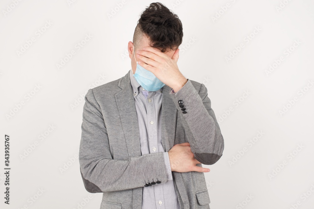 Indoor portrait of handsome man with stylish haircut, wearing casual clothes, making facepalm gesture while smiling, standing over gray background amazed with stupid situation. Indoor portrait of handsome man with stylish haircut, wearing casual clothes, making facepalm gesture while smiling, standing over gray background amazed with stupid situation.
