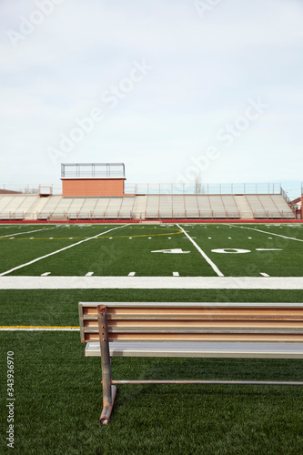 American football field with bench in foreground and empty bleachers in background
