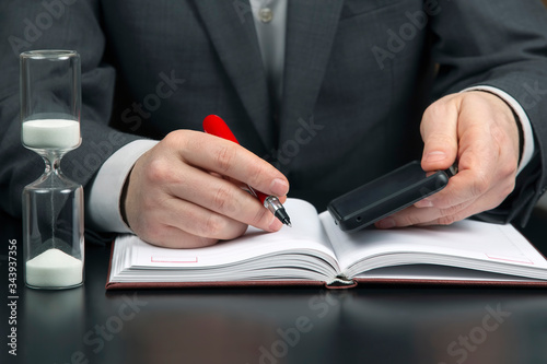 business man in the office is working with a mobile phone on the background of an hourglass. business and successful goal