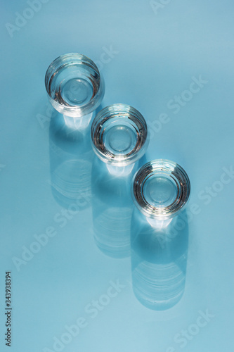Three glasses of water with soft shadows, top view, on a blue background. Freshness and purity, concept