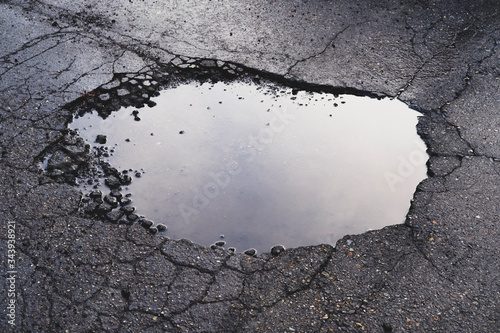 Water filled pothole on urban street with cracks and fracture marks