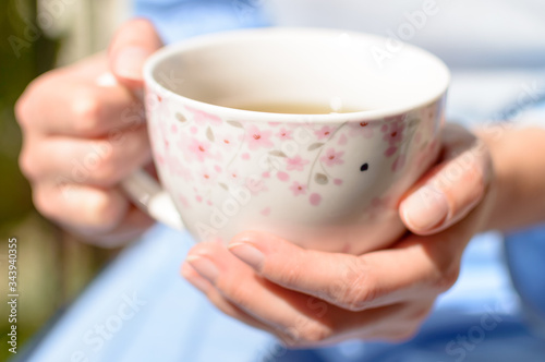A woman holds a cup of hot tea in her hands in the sunshine