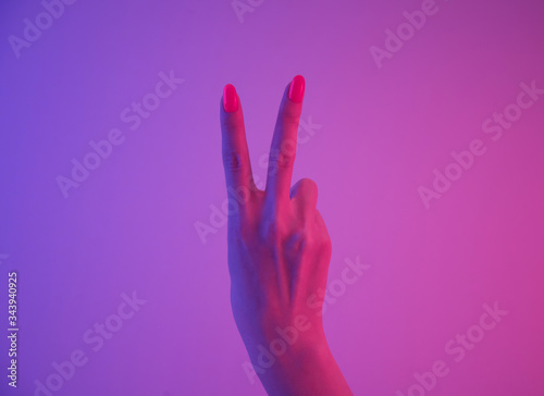 Female hand with orange manicure showing peace gesture in neon light.
