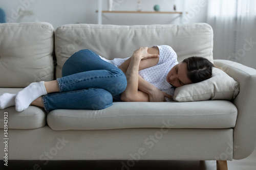 Depressed young woman lying on couch on living room feeling distressed lonely after breakup or divorce, upset unhappy millennial female mourn yearn on sofa, suffer after miscarriage or abortion photo