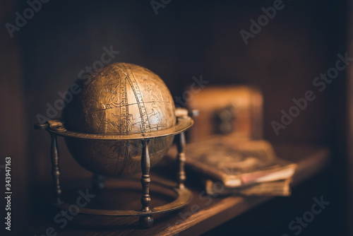 vintage globe made of copper, in the background a chest and books