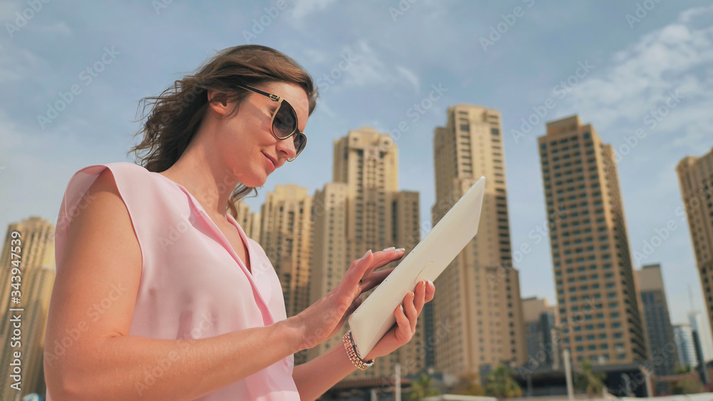 A girl works on a tablet against the background of skyscrapers of a metropolis. A girl works on a tablet against the background of skyscrapers of a metropolis.