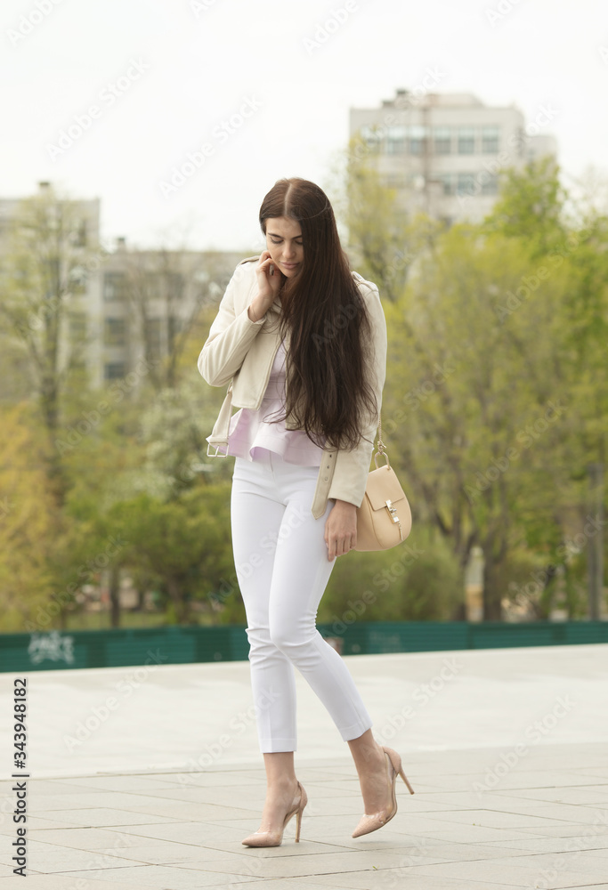 Obraz premium Fashion style portrait of young beautiful elegant brunette woman walking at city streets on a windy dull day.