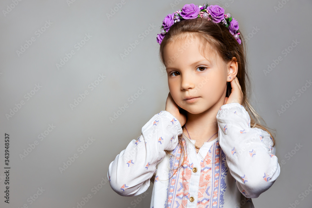 Portrait of posing pretty little girl in white dress and purple wreath on gray isolated background . Portrait of posing pretty little girl in white dress and purple wreath on gray isolated background .