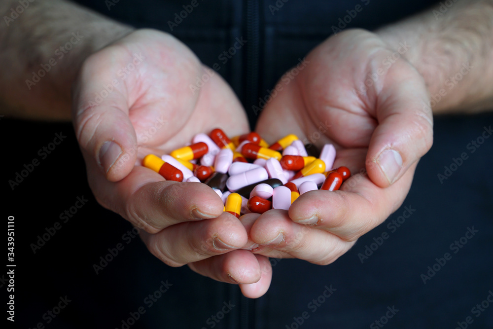 Closeup shot: hands of a young man holding colorful pills, vitamins, analgesics and antibiotics. Health support and treatment, medication, prescription drugs, vitamin tablets. 