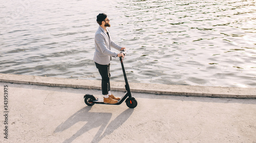 Young hipster man in a suit riding an electric scooter in bright sunny day. Ecological transportation concept.