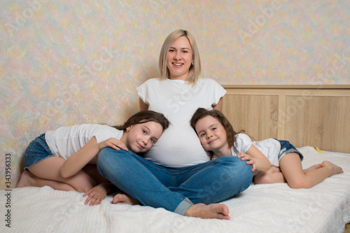 Maternity portrait of two beautiful little girls hugging their mother's pregnant belly. happy family. Kids love mother