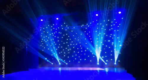 Blurred show background. Empty stage and sparkling stage lights. Blue light beams spotlights on stage at time of entertainment show. Laser and lights show in the dark
