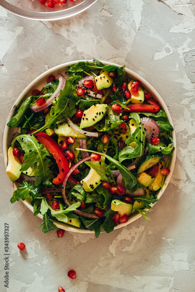Green vegetable salad with ruccola, pomegranate seeds, avocado, onions and herbs. Gray concrete background. Thyme. Vertical orientation