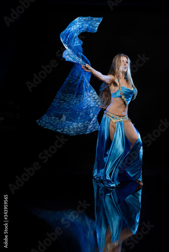 Young woman belly dancer in a blue oriental costume on a black background photo