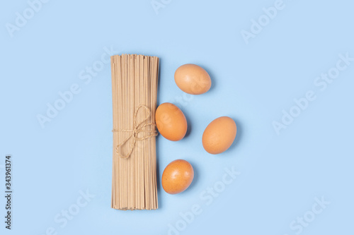 Uncooked whole grain spaghetti and eggs on a blue table. Cooking pasta.