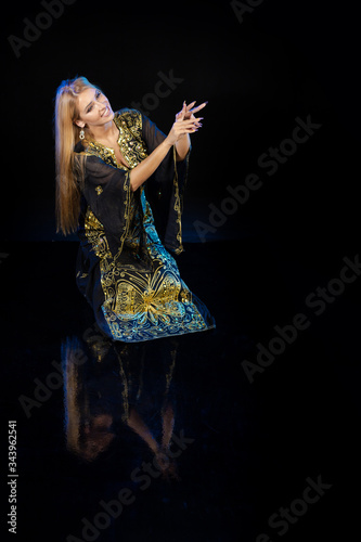 Young woman oriental dancer in national traditional Khaliji dress with feathers on a black background photo