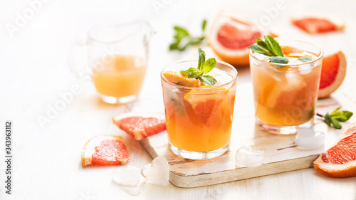 Grapefruit cocktails with mint and ice. Cold summer citrus fresh beverage on light wooden background