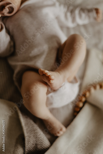 legs of a baby lying on a beige plaid and wooden toys on the background