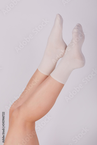 Female legs in white cotton socks on white background. Ladies wearing sports socks