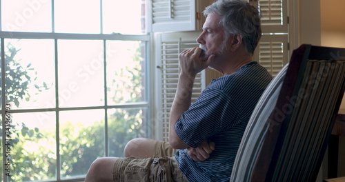 An older man stares out the window during coronavirus pandemic depressed about business closures and financial woes.