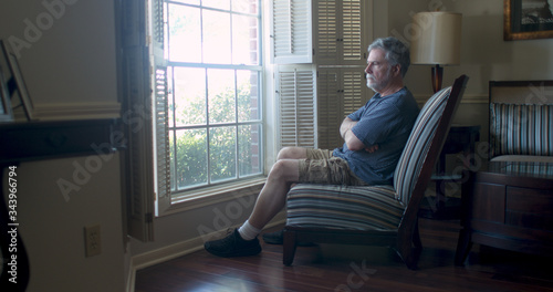 Depression setting in for this mature man sitting by his window feeling isolated and fearful during the coronavirus pandemic business closures as well as market woes.