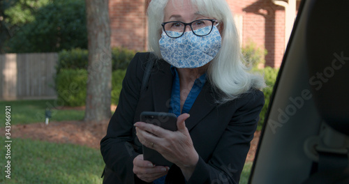 A mature woman Uber or Lyft ride sharing customer wearing a mask due to COVID19 risks greets the driver and checks the service app on her mobile phone before starting. photo