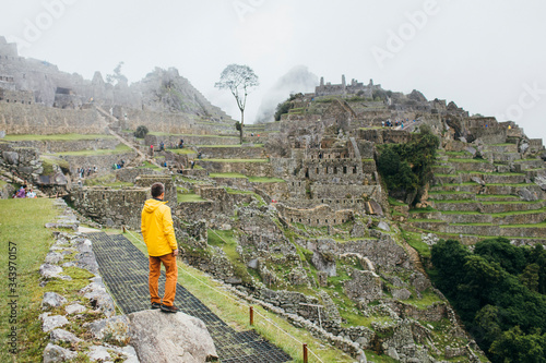 A man in a yellow jacket is standing near ruins of Machu Picchu, Peru photo