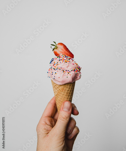 Hand holding strawberry ice cream cone against white background. photo